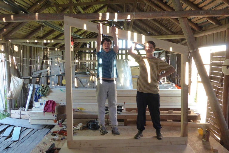 Zwei Personen in einer hellen Holzwerkstatt mit Holzbalkenkonstruktion und Holzrahmen