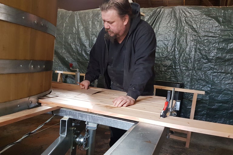 Mann arbeitet an einer Holzbadewanne in einer Werkstatt.