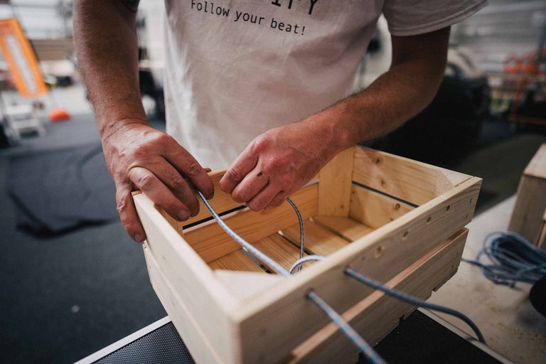 Un homme enfile un cordon élastique dans une caisse en bois