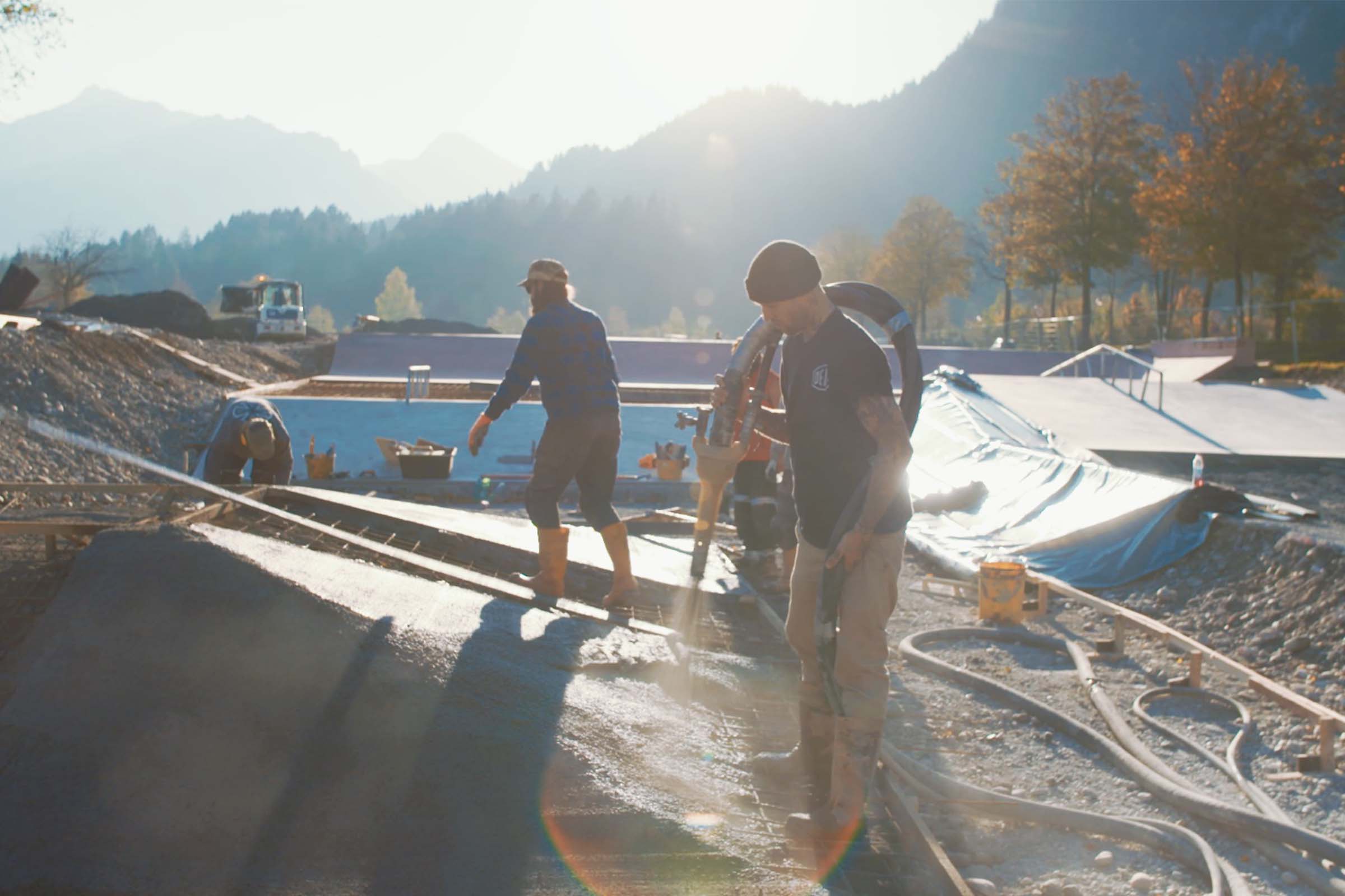 Ouvriers du bâtiment bétonnant un skatepark avec un panorama montagneux en arrière-plan