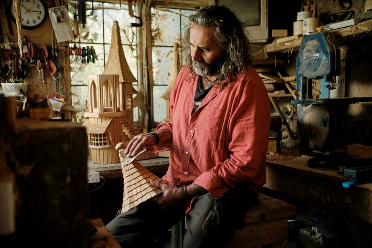 Un artisan est assis dans son atelier et travaille sur un nichoir en bois.