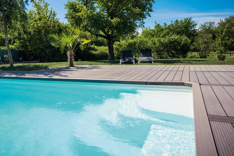 Scène avec une piscine, une terrasse en bois et deux chaises de jardin en arrière-plan