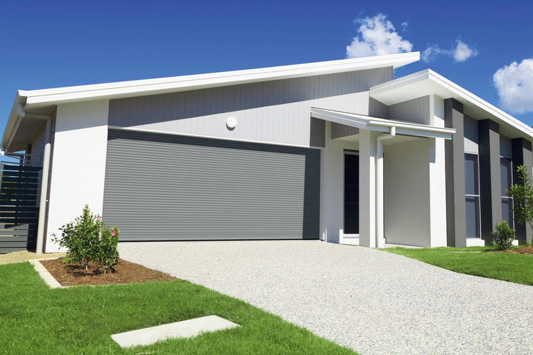 Ein modernes Haus mit einer grauen Rolltor Garage, einem gepflasterten Weg und einem gepflegten Garten.