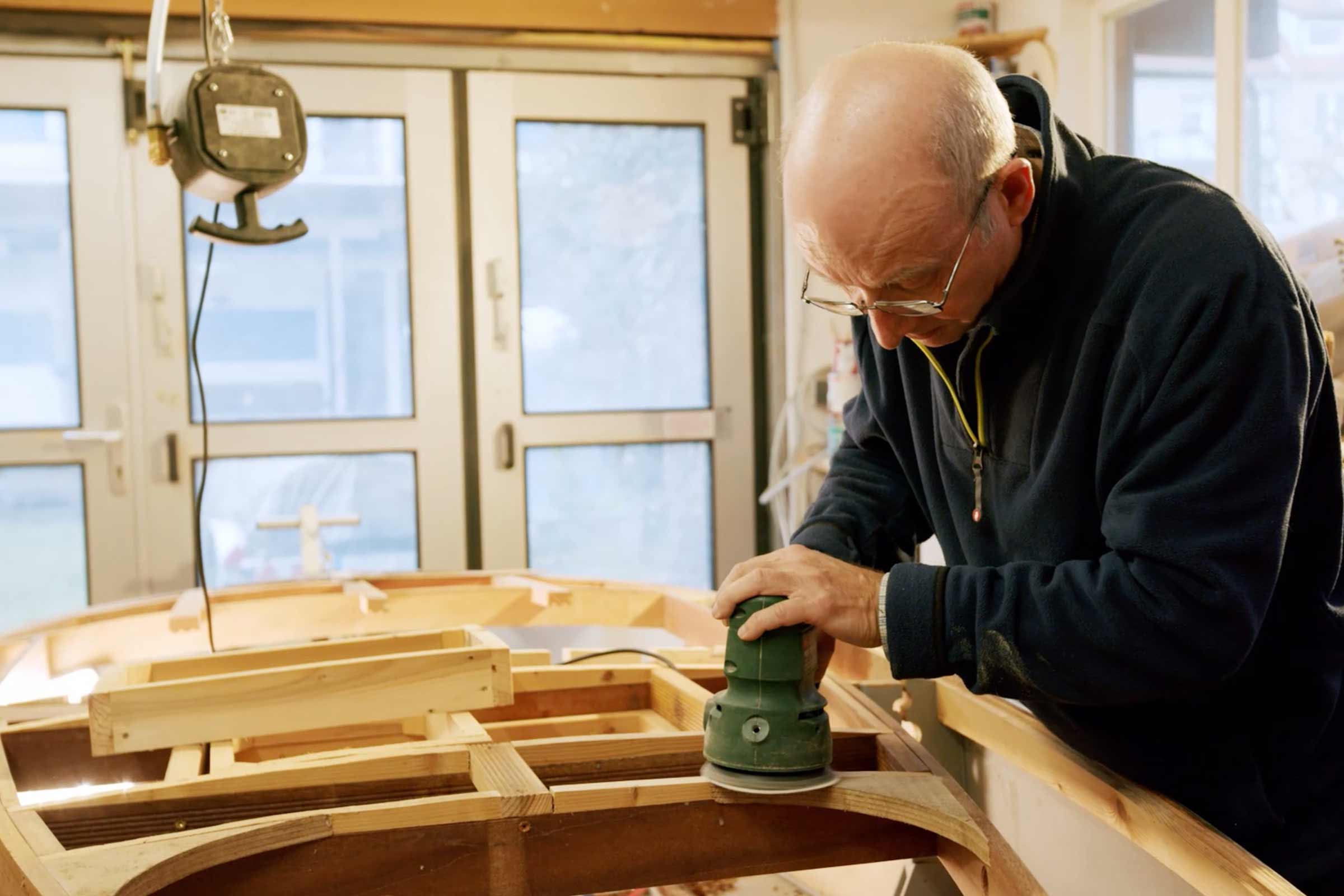 Un homme ponce du bois avec une ponceuse excentrique dans un atelier.