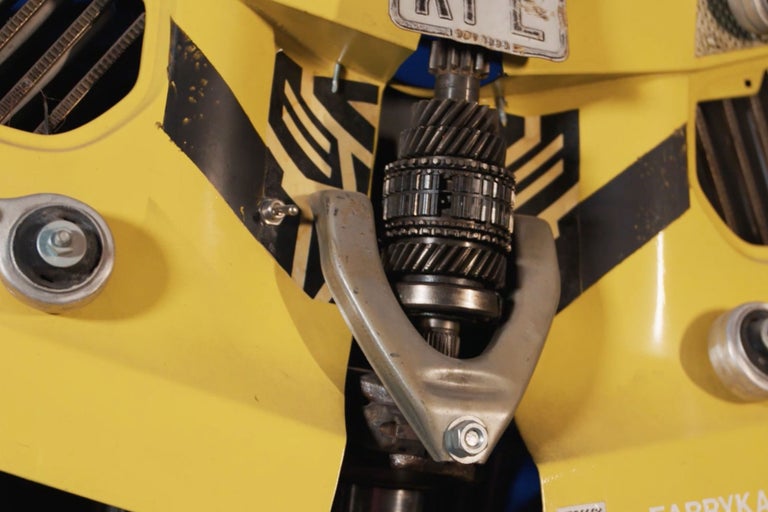 Gros plan d'une pièce de véhicule jaune avec des engrenages et un support argenté.