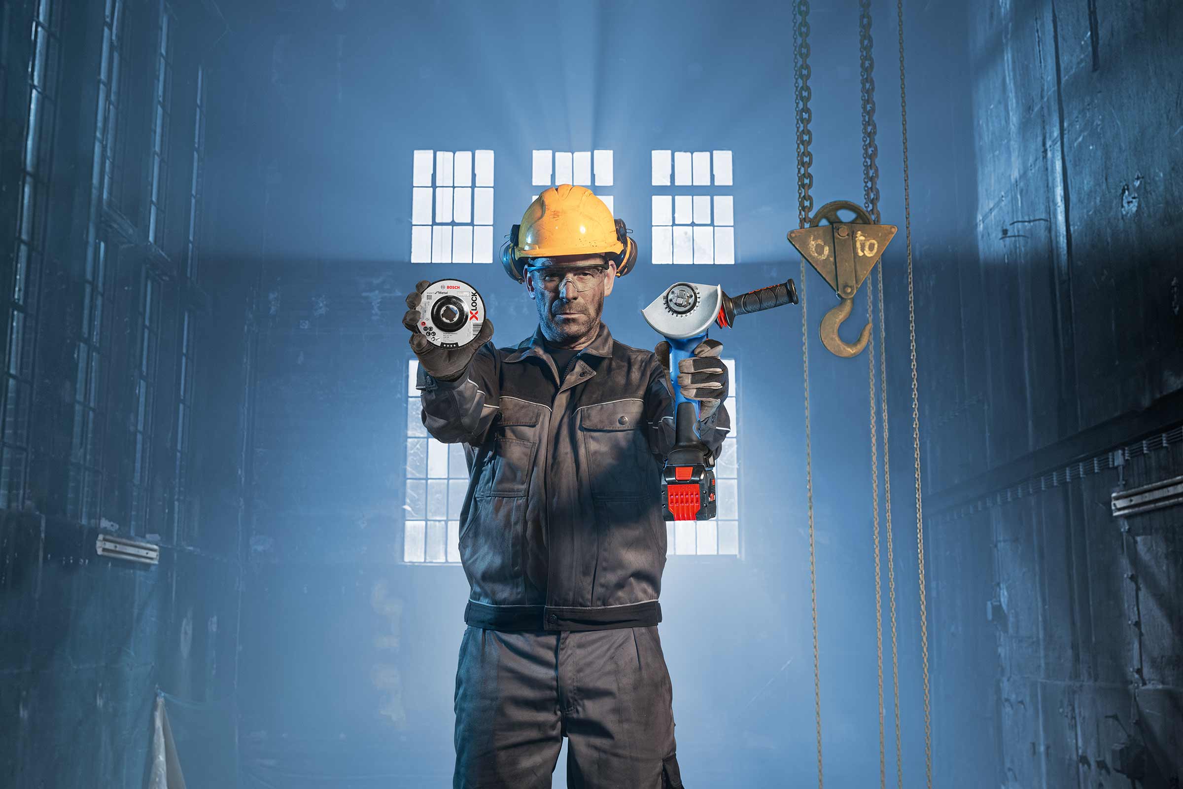 Un homme portant un casque et des lunettes de protection tient un disque à tronçonner et une meuleuse d'angle sans fil.