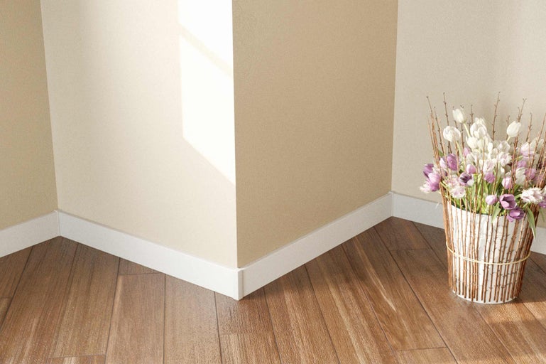 Vue d'angle d'une pièce avec plancher en bois, plinthes blanches et un vase de fleurs