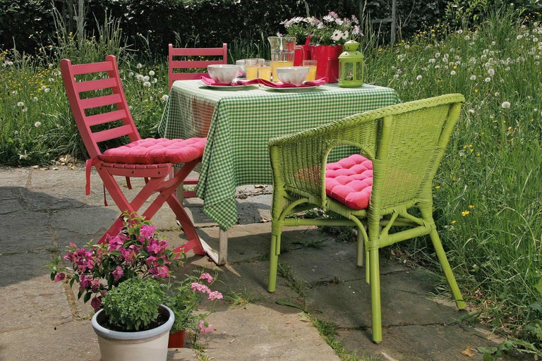 Gartenszene mit Tisch, karierter Tischdecke, Geschirr, Getränken und Stühlen mit Sitzkissen