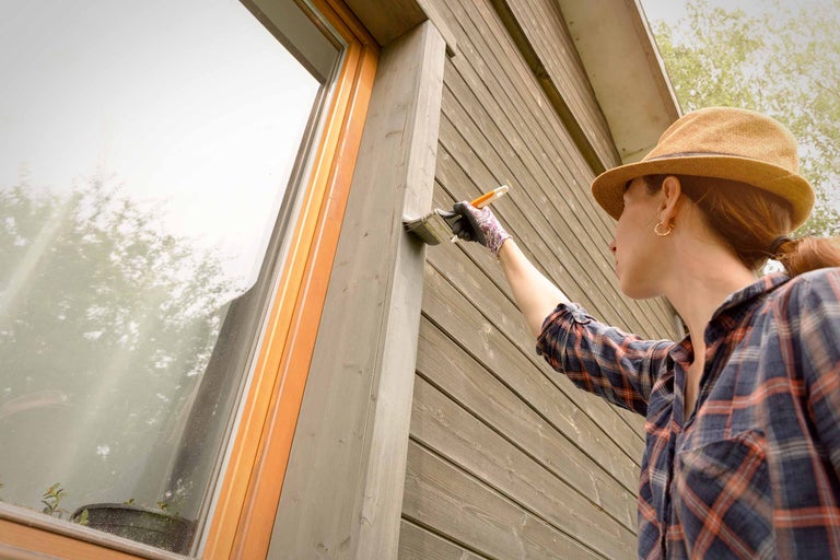 Femme peint une façade en bois avec un pinceau