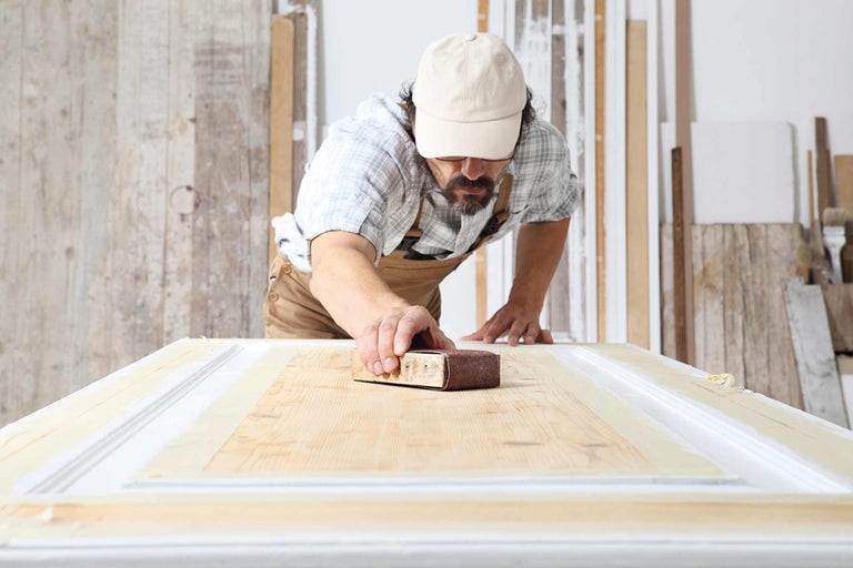 Homme ponçant une porte en bois avec du papier de verre