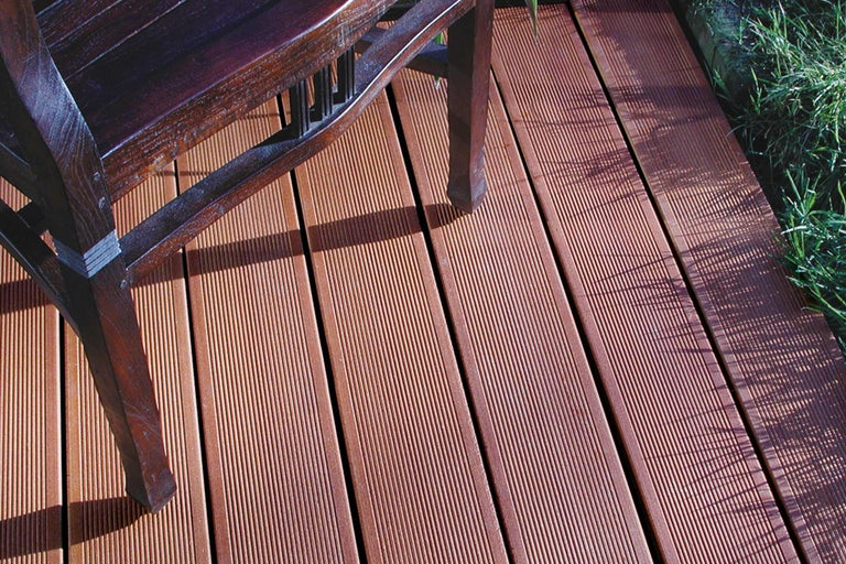 Lames de terrasse en bois avec une surface rainurée et un pied de chaise sur l'image.