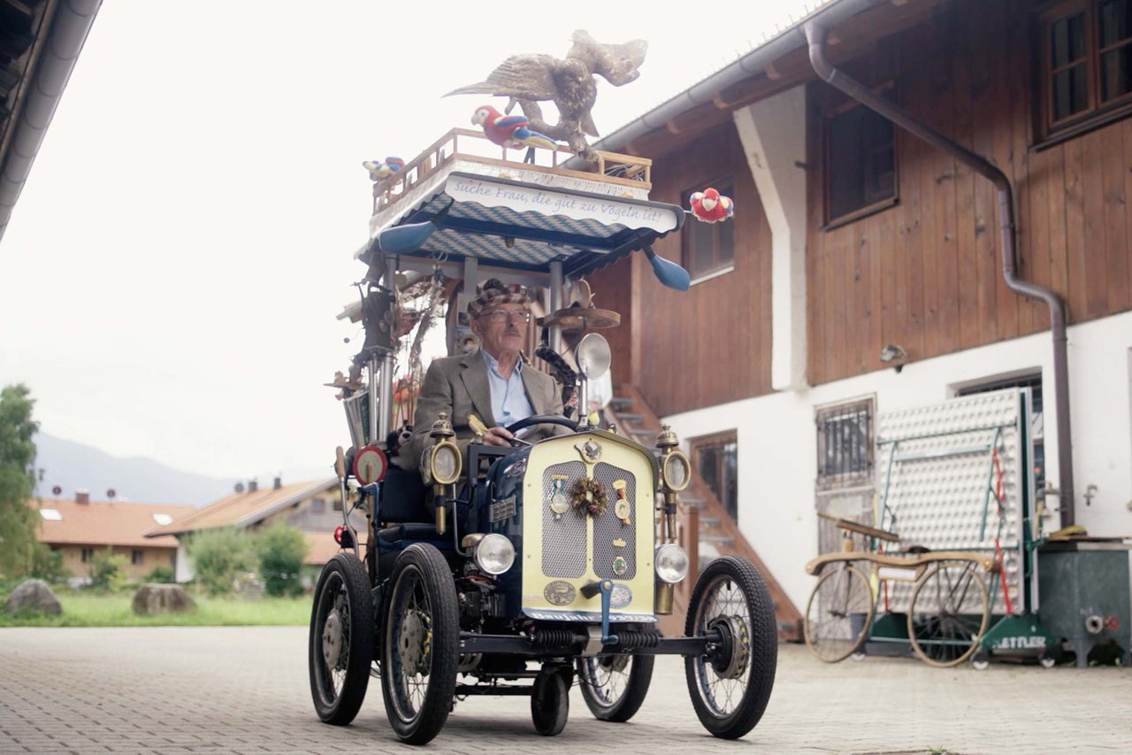 Un homme conduit une voiture décorée avec des motifs d'oiseaux devant une maison.