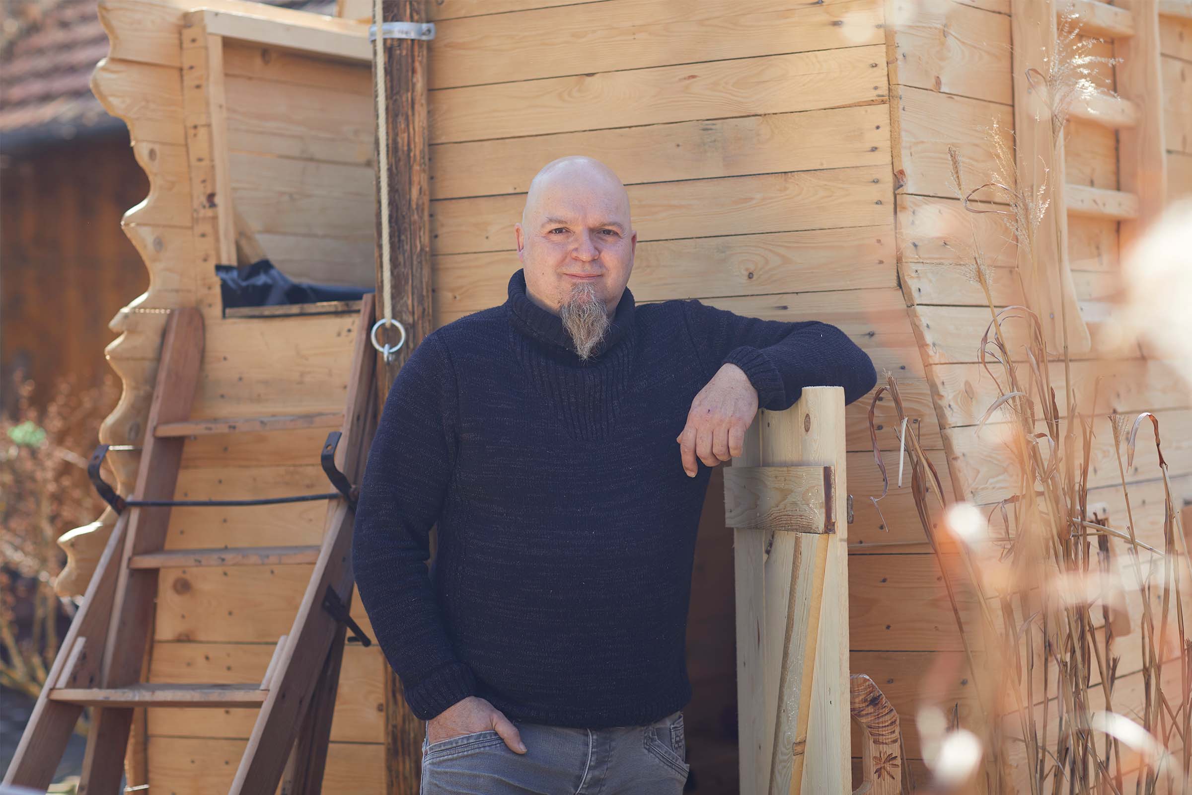 Un homme se tient devant une maison en bois avec une échelle.