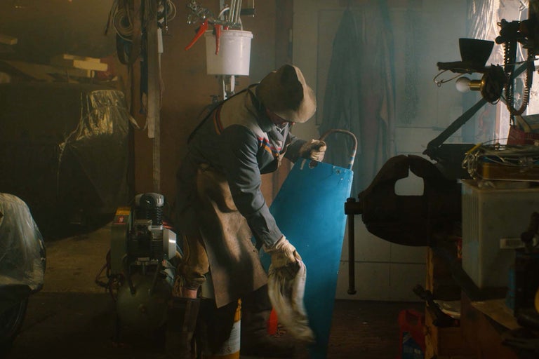 Scène d'atelier avec une personne nettoyant une plaque métallique bleue, entourée d'outils et d'équipements.