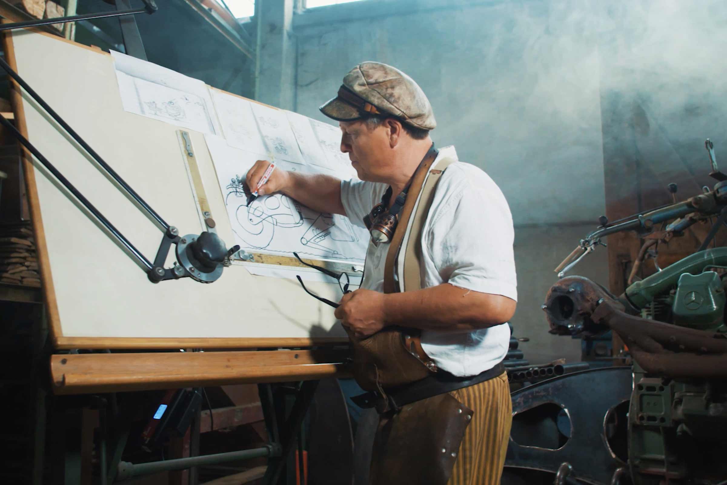 Un homme dessine des dessins techniques sur une table à dessin avec du matériel de dessin dans une pièce lumineuse.