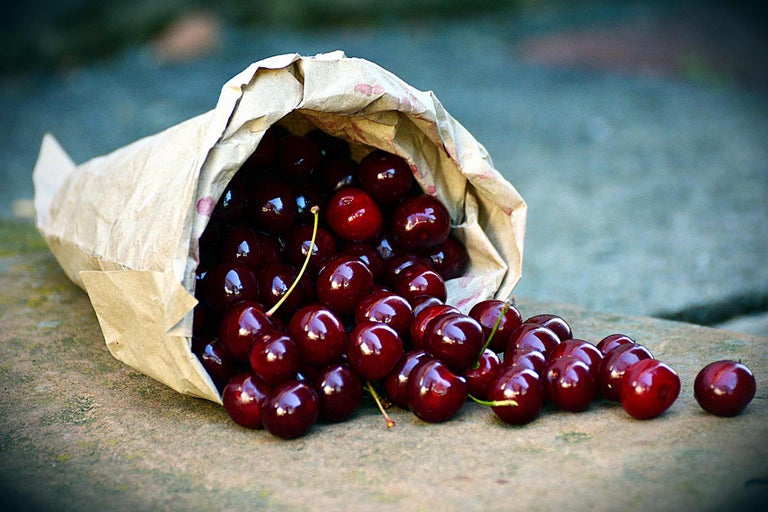 Un sac en papier contenant des cerises repose sur une surface