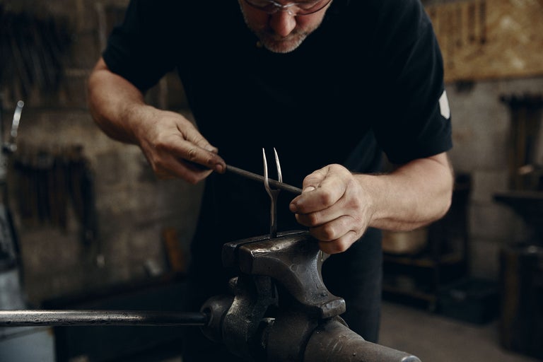 Un homme travaille le métal avec une lime dans un étau. Ferronnerie.