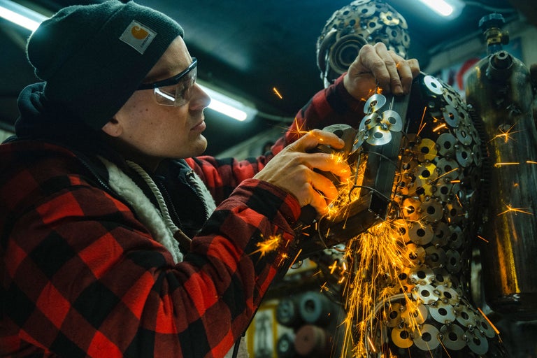 Artisan travaillant une construction métallique avec une meuleuse d'angle, des étincelles jaillissent.