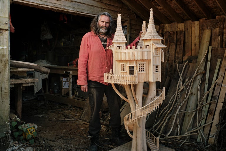 Homme se tenant à côté d'un modèle de cabane dans les arbres en bois dans un atelier