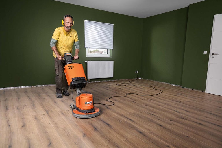 Un homme utilise une ponceuse à parquet dans une pièce avec un sol stratifié.