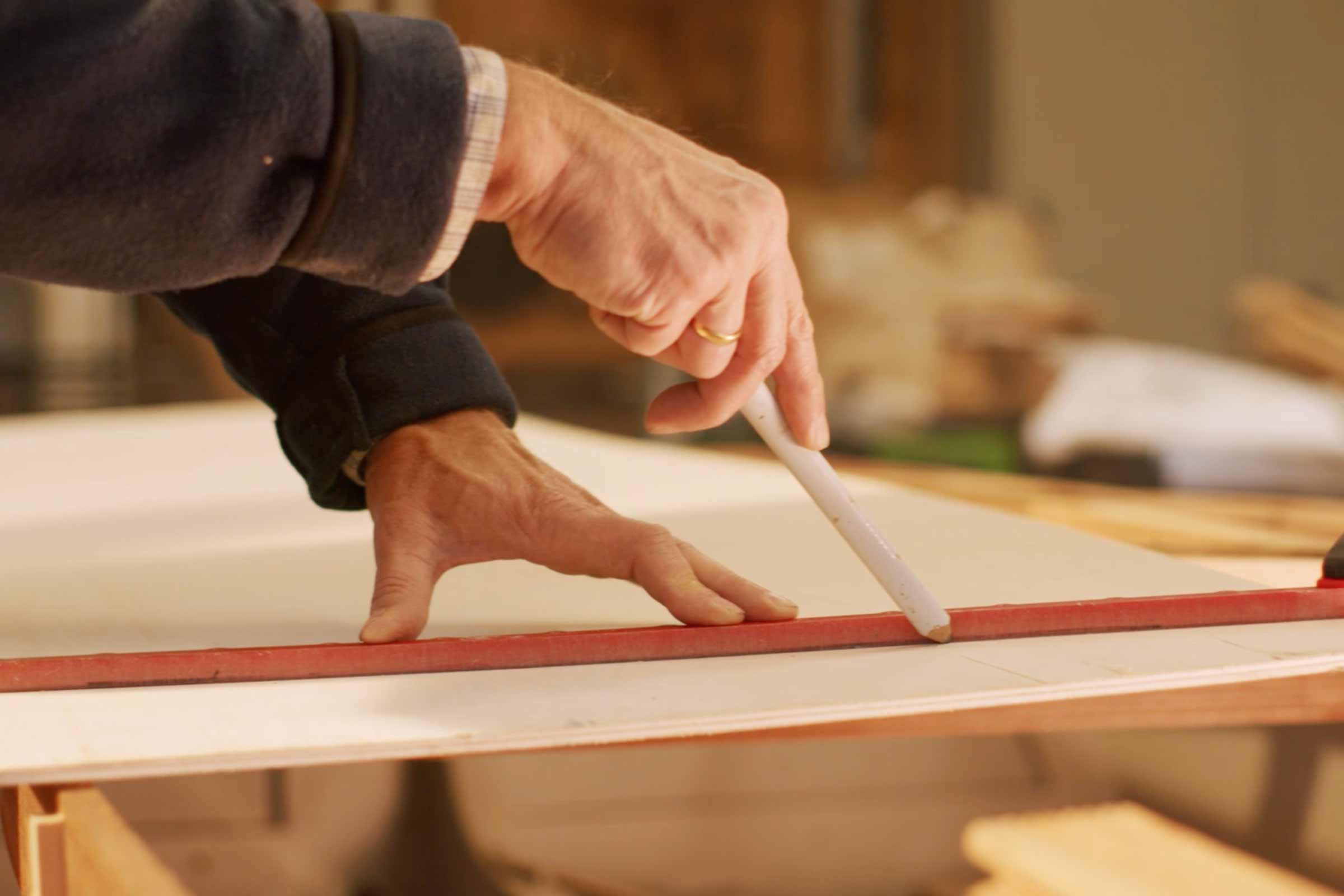 Un artisan trace une ligne sur une plaque de bois à l'aide d'une règle et d'un crayon.