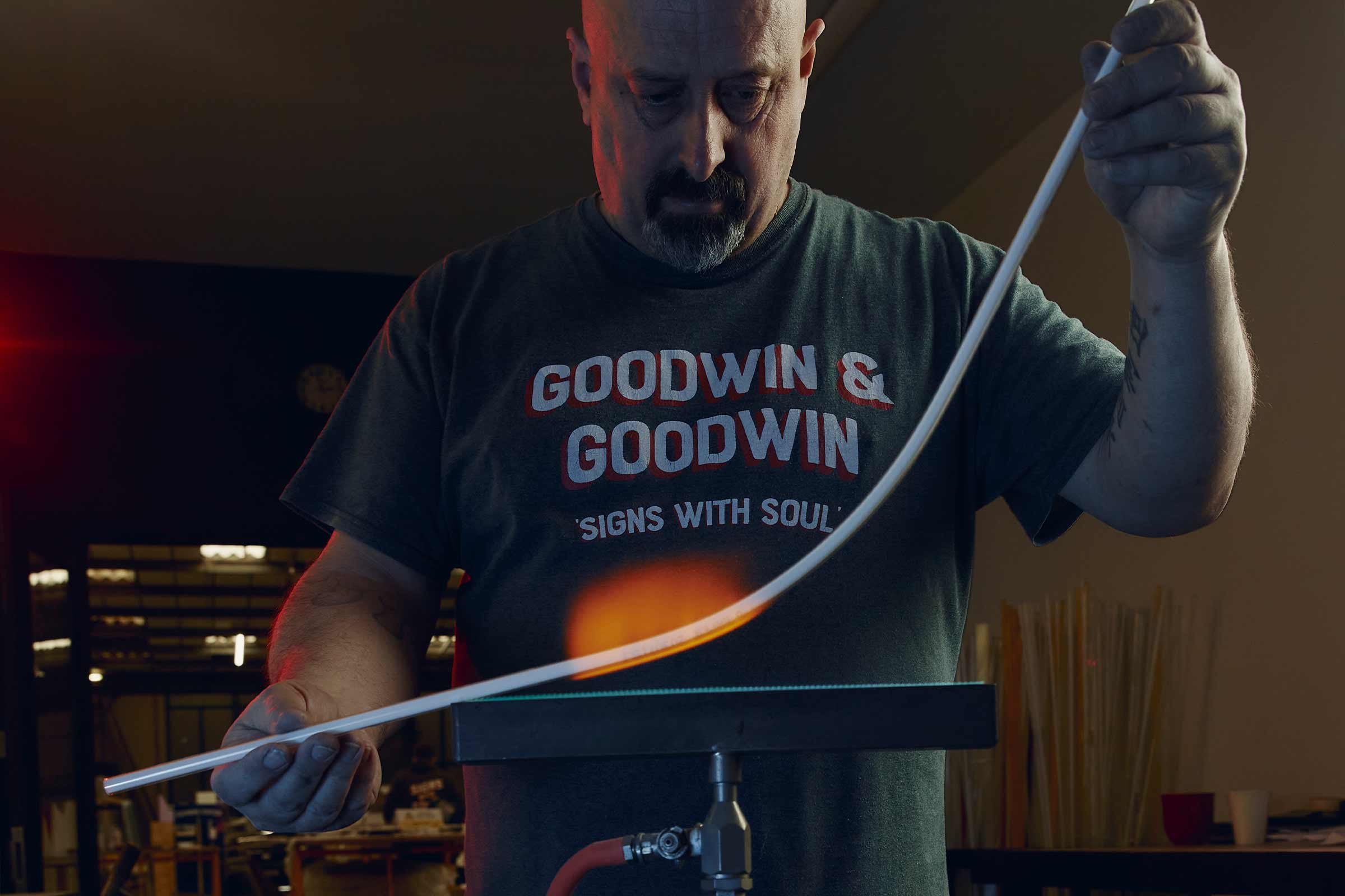 Un homme plie un tube de verre avec une flamme pour la fabrication d'enseignes lumineuses.