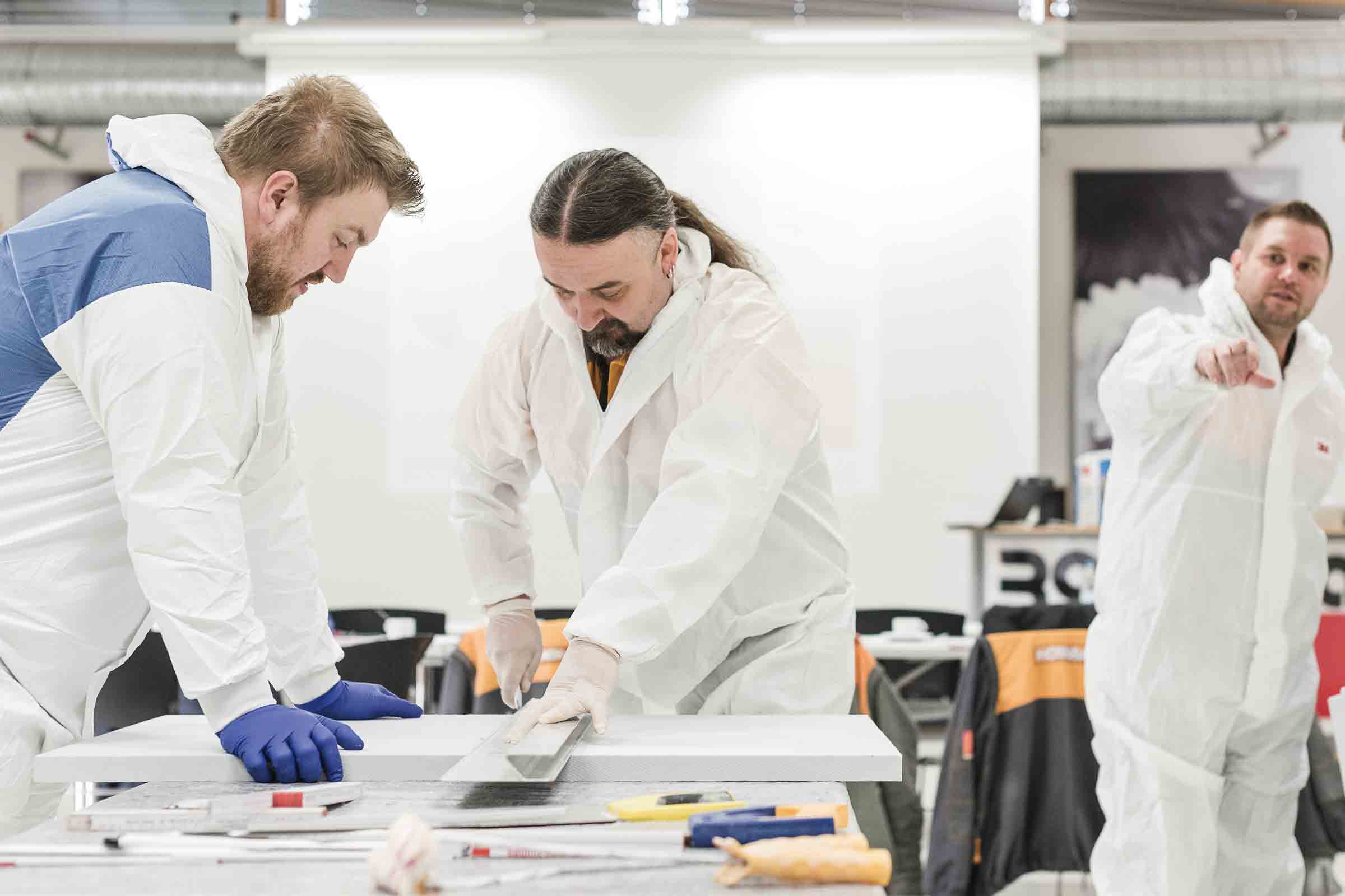 Trois artisans en combinaison de protection travaillent une surface blanche avec des outils