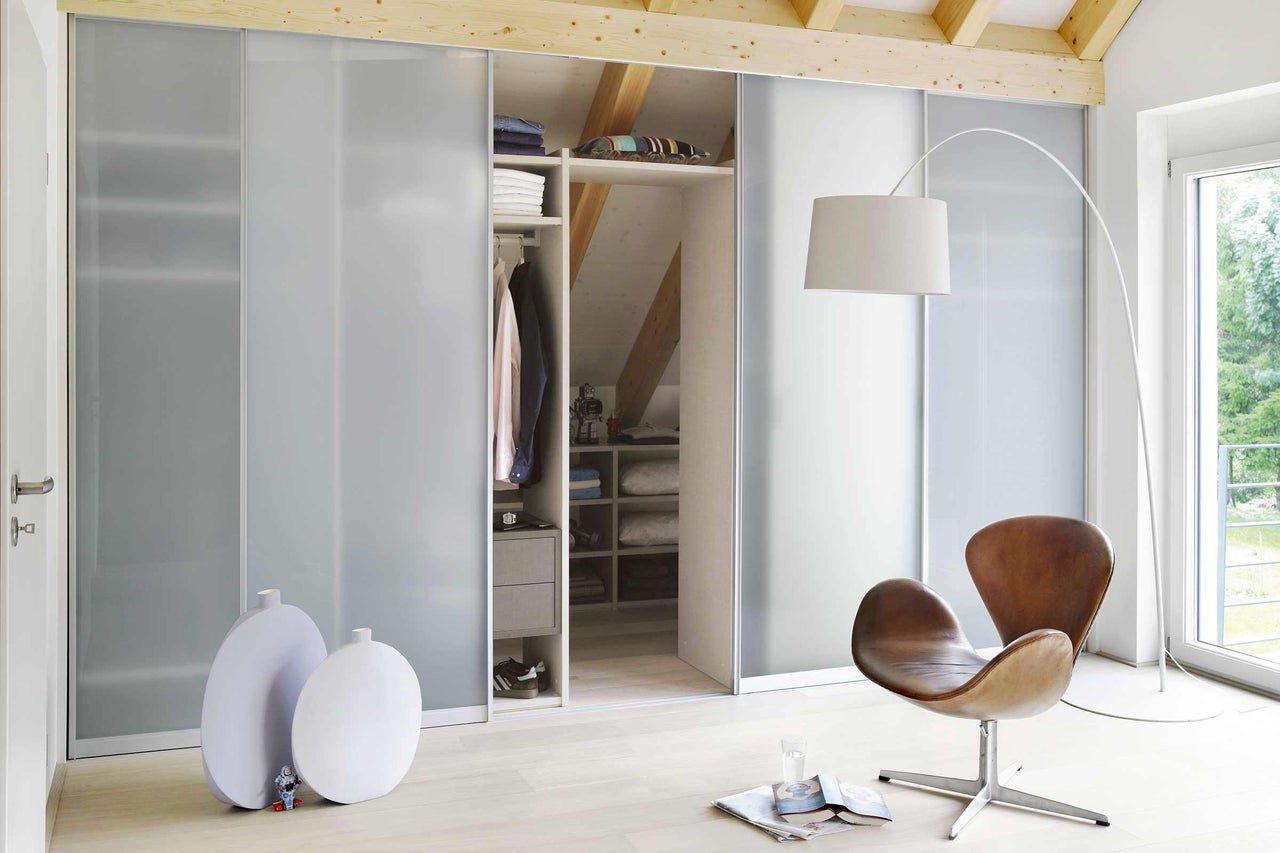 Begehbarer Kleiderschrank mit Schiebetüren in Dachgeschosszimmer mit Lampe und Sessel