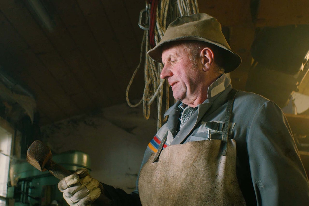 Un homme avec un chapeau, un tablier et des gants tient un marteau à la main