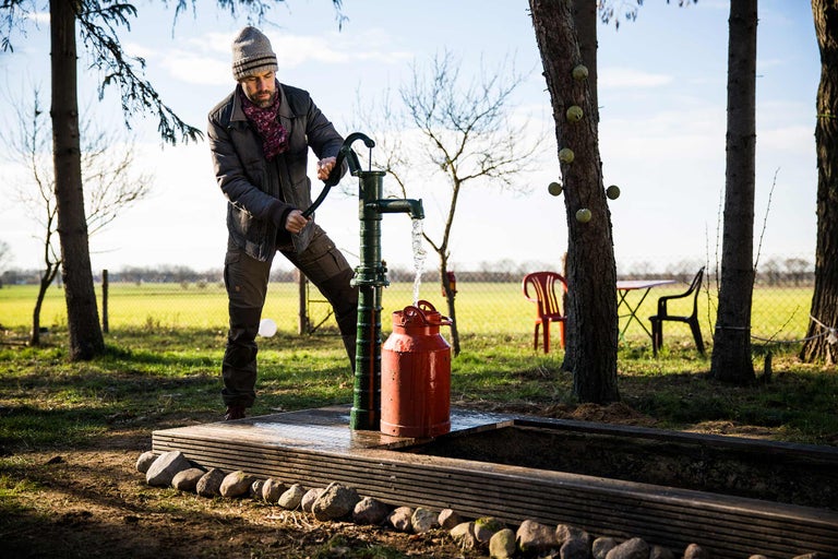 Mann betätigt eine Gartenpumpe im Freien und füllt einen Eimer mit Wasser.