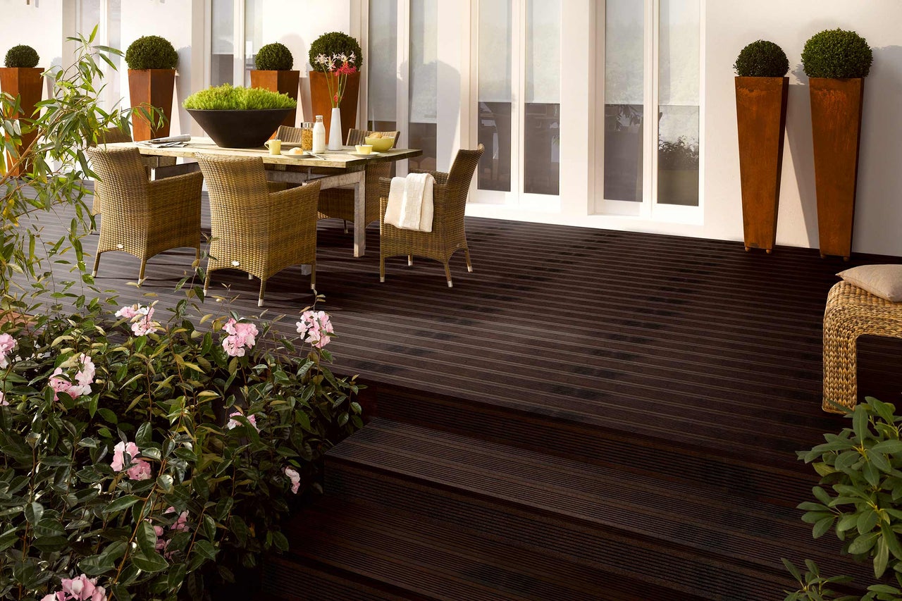 Terrasse mit dunklen Holzdielen, Gartenmöbeln und Pflanzen