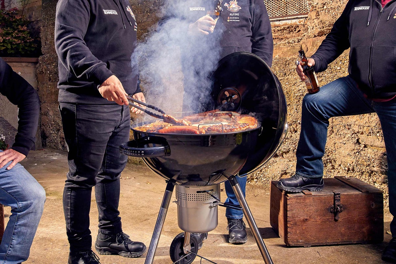 Gruppe von Personen grillt auf einem Holzkohlegrill mit verschiedenen Fleischsorten und Würstchen