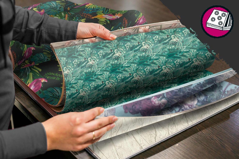 Eine Person blättert in einem Tapetenmusterbuch mit verschiedenen floralen und tropischen Designs.