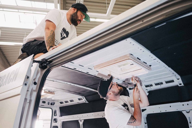 Deux hommes installent une fenêtre de toit dans un camion.