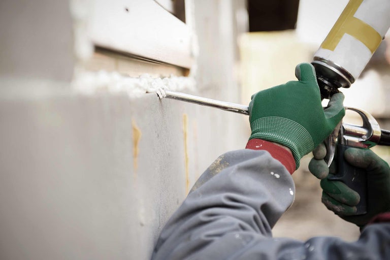 Ein Arbeiter trägt Handschuhe und verwendet Bauschaum, um ein Fenster abzudichten.