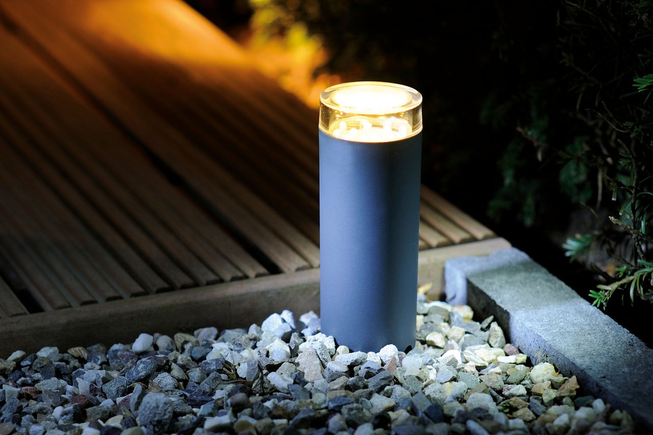 Luminaire de jardin cylindrique éclairé sur un chemin de gravier