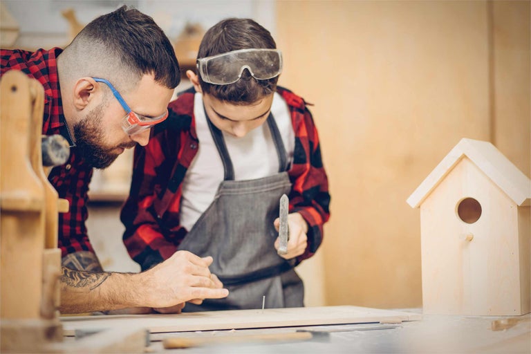 Père et fils construisent ensemble une cabane à oiseaux avec un marteau et un clou.