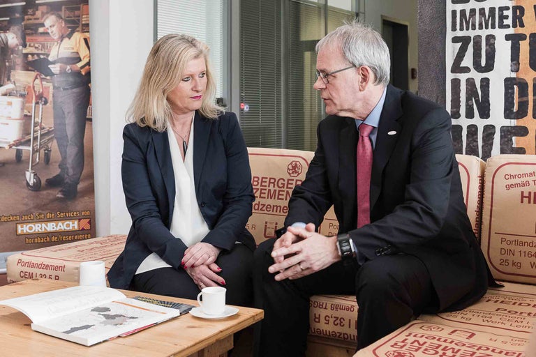 Deux personnes assises sur des sacs de ciment à une table avec une brochure et une tasse de café.