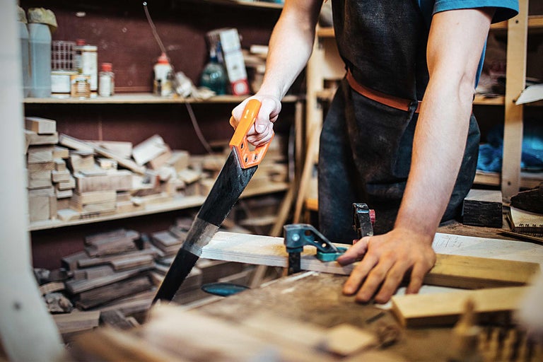 Handwerker sägt Holz mit einer Handsäge in einer Werkstatt.