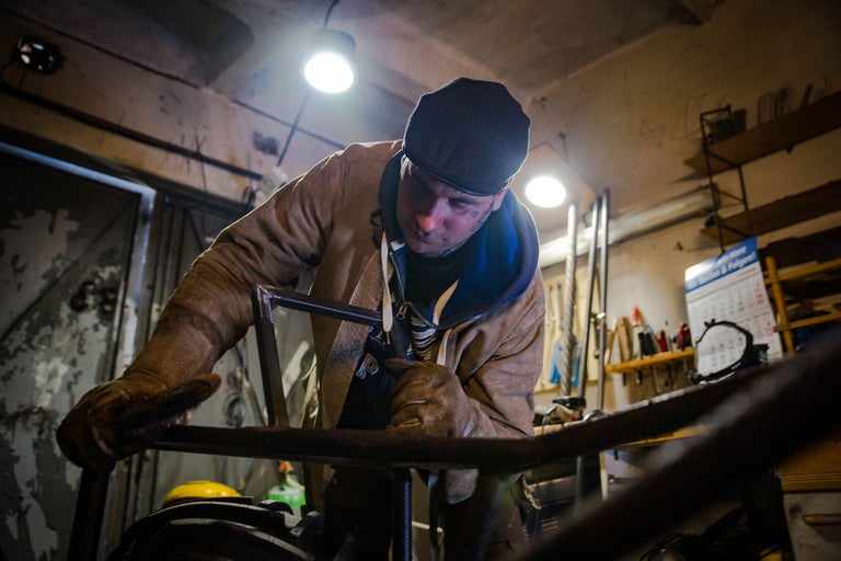 Un homme portant des vêtements de travail et des gants travaille sur une construction métallique dans un atelier.
