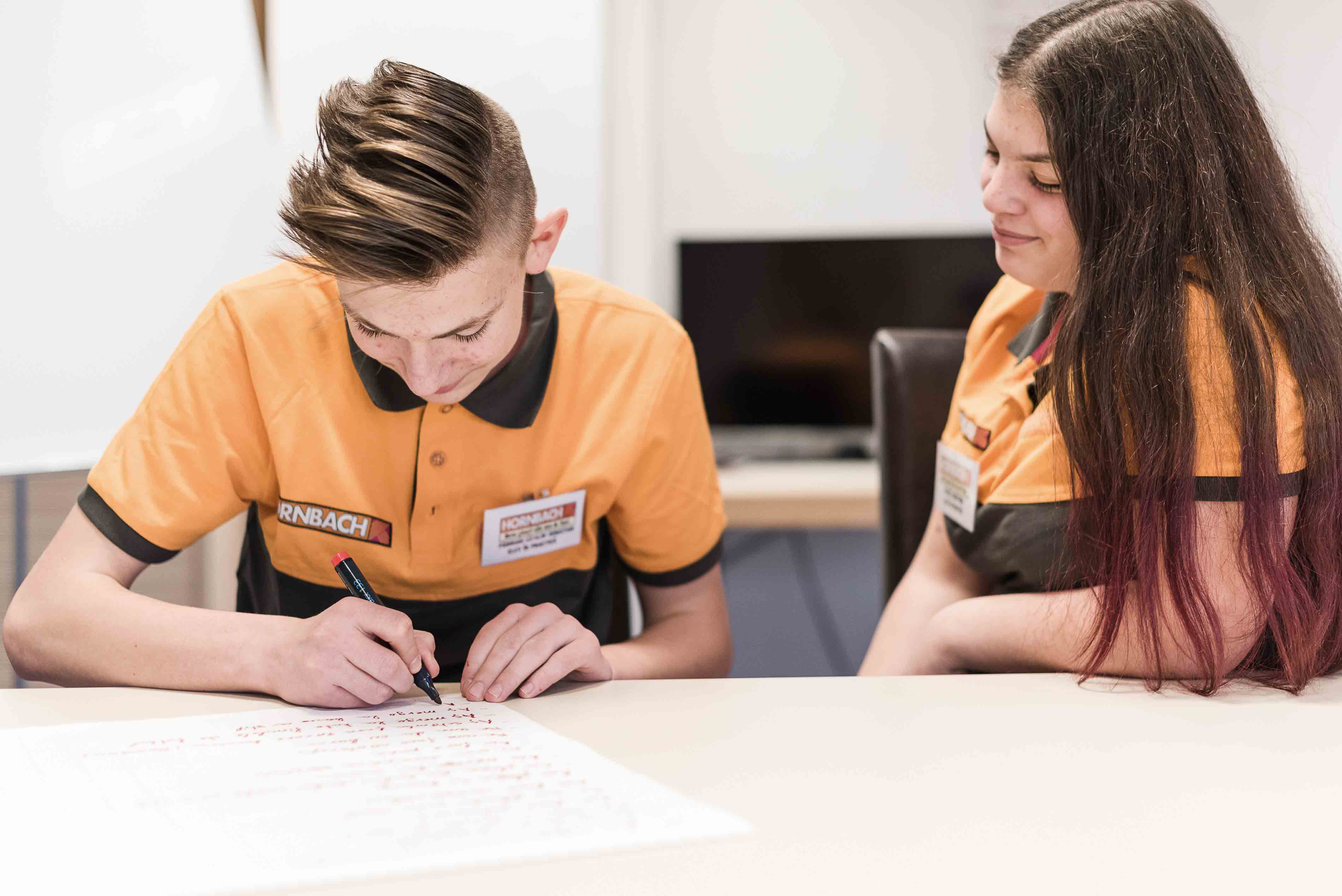 Deux collaborateurs de Hornbach sont assis à une table. L'un d'eux écrit quelque chose sur une feuille de papier.
