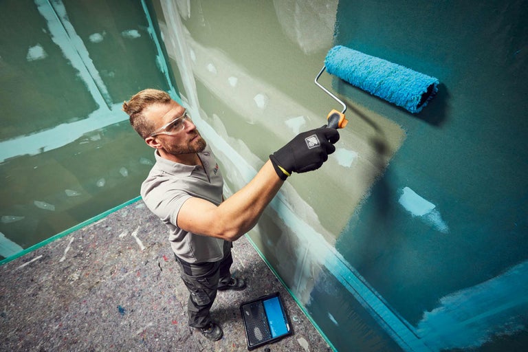 Un homme peint un mur avec un rouleau à peinture. Travaux de peinture à l'intérieur.