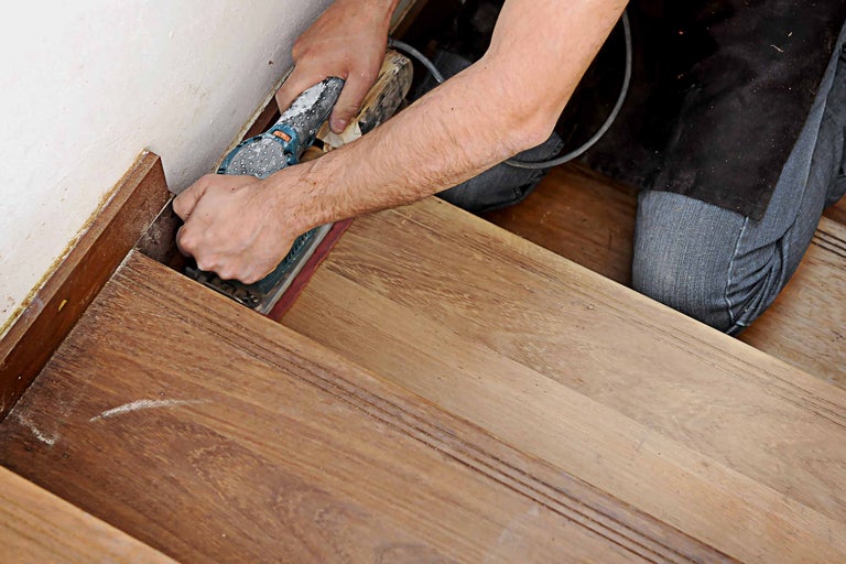 Artisan ponçant un escalier en bois avec une ponceuse vibrante.