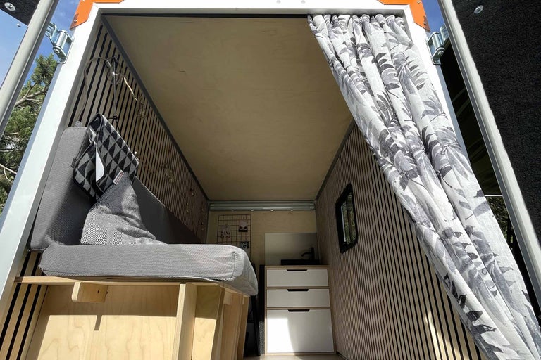 Aménagement intérieur d'une camionnette avec lit, rideaux et espace de rangement