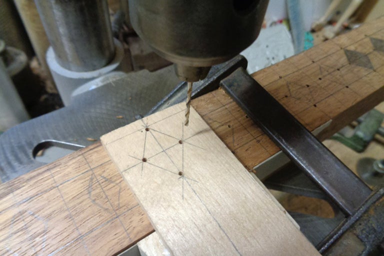 Gros plan d'une perceuse perçant des trous dans une planche de bois fixée avec un serre-joint.