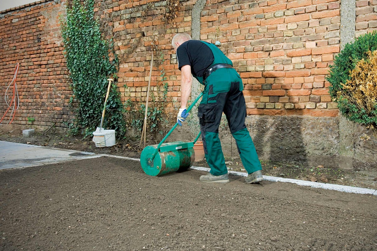 Une personne utilise un rouleau de jardin pour tasser la terre.