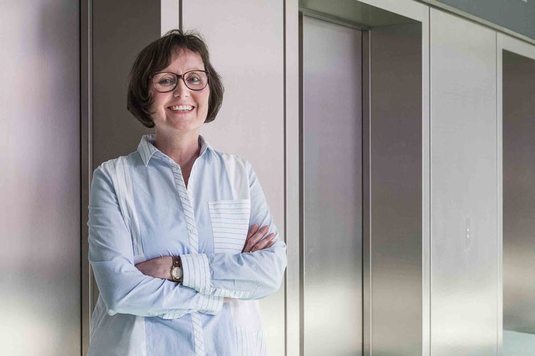 Portrait d'une femme devant des ascenseurs, elle porte un chemisier rayé