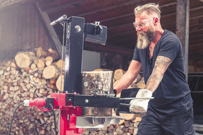 Mann spaltet Holz mit einem Holzspalter in einem hellen Arbeitsbereich