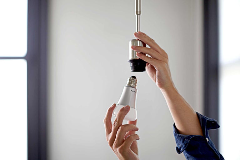 Une personne visse une ampoule Philips dans une douille de lampe.