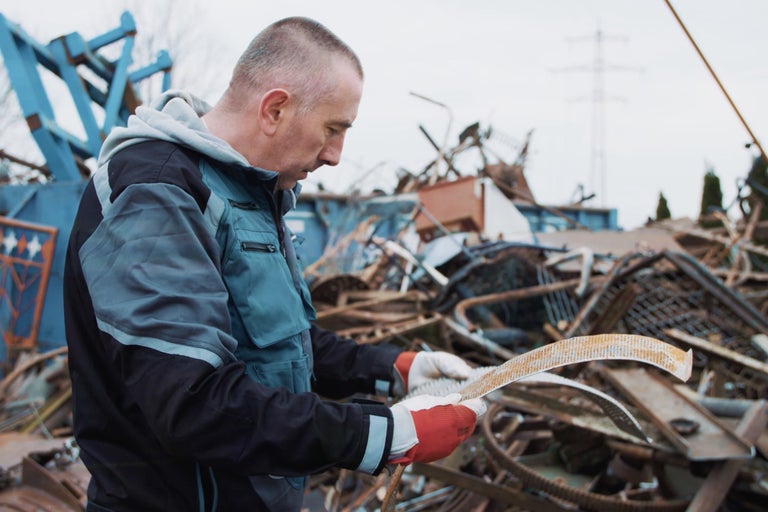 Homme en vêtements de travail examinant de la ferraille devant une casse